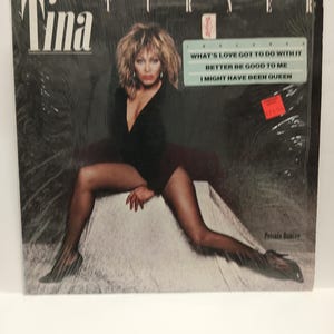 May include: A vinyl record album cover featuring Tina Turner. The album cover has the name "Tina" in large white letters. The album title "Private Dancer" is visible. The track list includes "What's Love Got to Do with It".