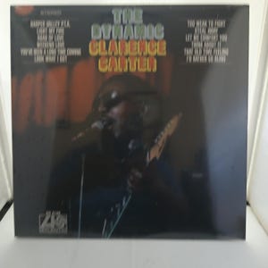 May include: Album cover for "The Dynamic Clarence Carter." The album features a photo of Clarence Carter singing and playing a guitar. The album title is in large, colorful letters. Song titles are listed on the left and right sides of the cover.