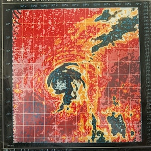 May include: A colorful weather map with a grid overlay, depicting a hurricane or tropical storm. The image features a vibrant palette of reds, oranges, blues, and blacks, with temperature gradients. The map includes latitude and longitude markings.