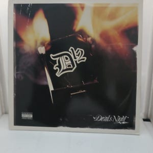 May include: Album cover for D12's "Devil's Night." The album art features the D12 logo in a stylized font, set against a dark background with flames. The album title is written in a cursive font at the bottom.