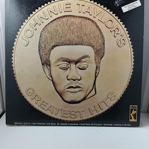 May include: A vintage vinyl record album titled "Johnnie Taylor's Greatest Hits." The album cover features a gold-colored portrait of Johnnie Taylor. The album's tracklist is listed at the bottom. The album is marked "For Demonstration Use Only Not For Sale."