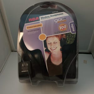 Puede incluir: Auriculares inalámbricos RCA en un embalaje de plástico transparente. El embalaje presenta a una mujer con los auriculares y el texto "¡Libertad de cables!". Los auriculares son negros y el embalaje tiene detalles en morado y blanco.