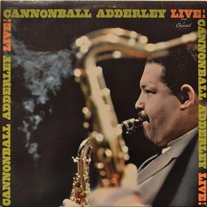 Może przedstawiać: Okładka albumu "Cannonball Adderley Live!" przedstawiająca profil mężczyzny grającego na saksofonie. Tytuł albumu i nazwisko artysty są w żółtym i pomarańczowym tekście. Widoczne jest logo Capitol Records.