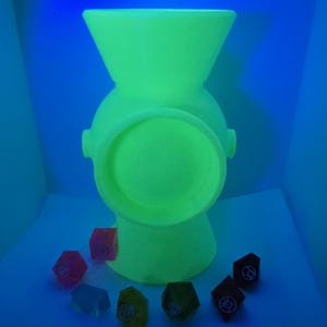 May include: A green glow-in-the-dark plastic model of a Green Lantern power battery with six multi-colored dice in front of it.