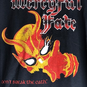 May include: Black t-shirt with a red and yellow graphic of a demon's head with horns and the text "Mercyful Fate" and "don't break the oath."