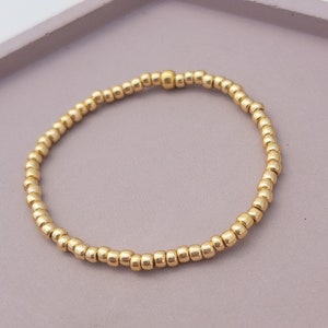 May include: A gold beaded bracelet with a small gold bead accent. The bracelet is made of tiny, round beads that are strung together to form a simple, elegant design.