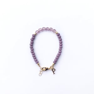 May include: A purple beaded bracelet with a gold clasp and a gold charm with the letter "P".
