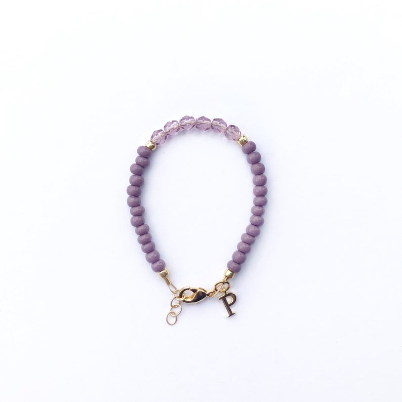 May include: A purple beaded bracelet with a gold clasp and a gold charm with the letter "P".