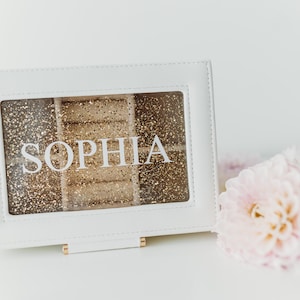 K&ouml;nnte beinhalten: Wei&szlig;e Schmuckschatulle mit goldfarbenem Glitzer-Innenraum und dem Namen "Sophia" auf der Vorderseite.