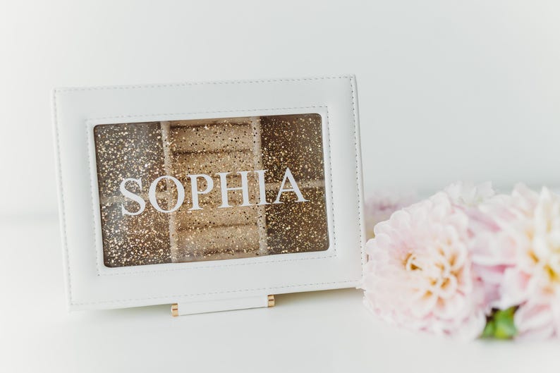 K&ouml;nnte beinhalten: Wei&szlig;e Schmuckschatulle mit goldfarbenem Glitzer-Innenraum und dem Namen "Sophia" auf der Vorderseite.