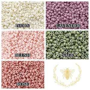 May include: Assortment of small round beads in various colours, including ivory, lavender, blush, sage, and rose. The beads are arranged in a grid pattern with the colour names written below each section. A small bee illustration with a wreath is in the bottom right corner.