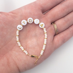 May include: White beaded bracelet with gold letters spelling out the name "LYDIA".
