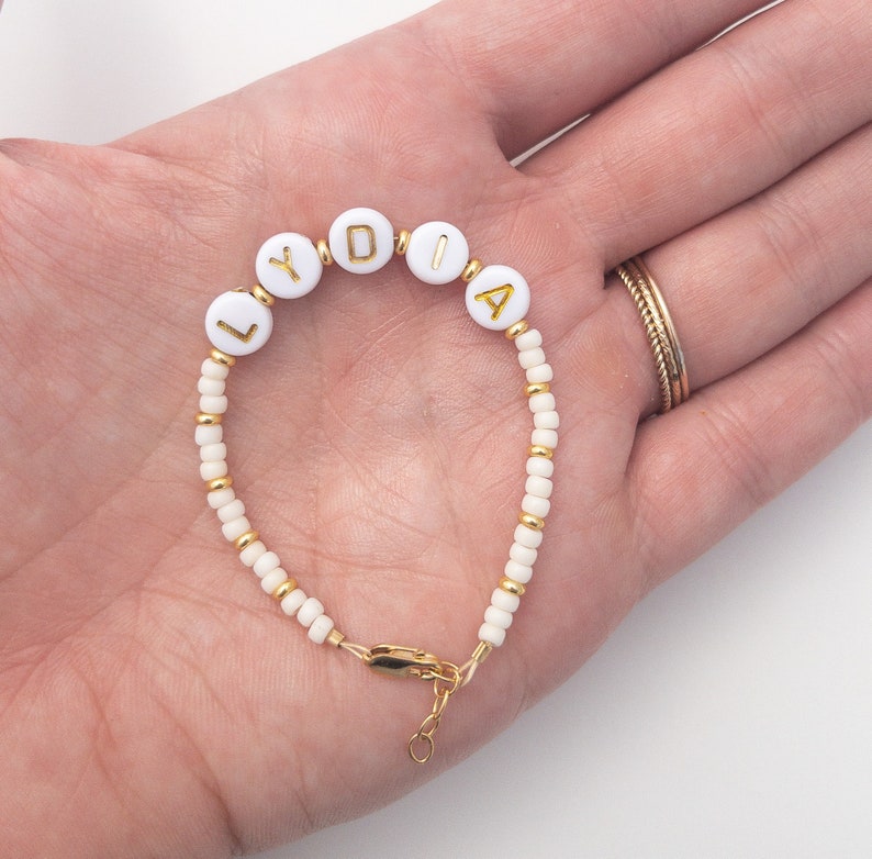 May include: White beaded bracelet with gold letters spelling out the name "LYDIA".
