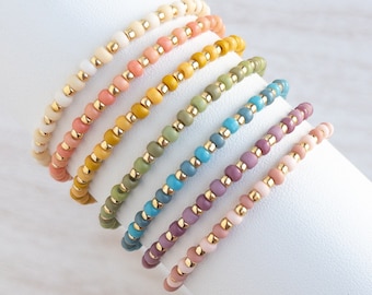 May include: A set of eight beaded bracelets in various pastel colors, including white, peach, yellow, green, blue, purple, and pink. The bracelets are made with small, round beads and have a delicate, feminine look.
