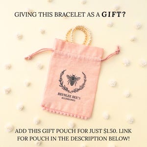 May include: A pink velvet pouch with a drawstring closure and a bee logo. The pouch is decorated with a white pom-pom trim. The text "Brynlee Bee's Accessories" is printed on the pouch.  "ADD THIS GIFT POUCH FOR JUST &pound;1.50. LINK FOR POUCH IN THE DESCRIPTION BELOW!" is written below the pouch.