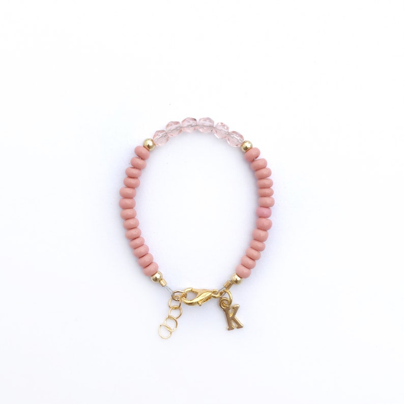 May include: A pink beaded bracelet with a gold clasp and a gold letter 'K' charm.
