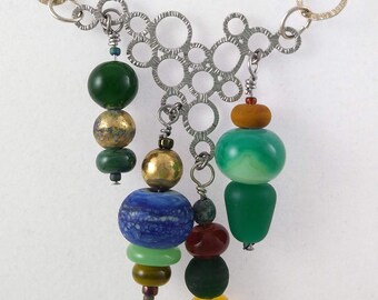 May include: A silver chain necklace with a geometric pendant featuring a cluster of circles. The pendant is adorned with a variety of colorful glass beads, including green, blue, gold, and amber.