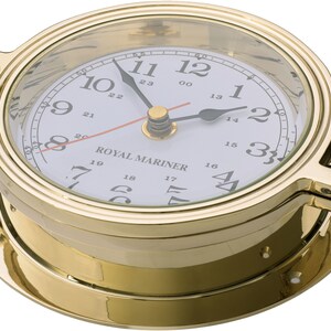 May include: A brass ship's clock with a white face and black hands. The clock has a glass cover and a brass bezel. The clock face has the numbers 1 through 12 and the words "ROYAL MARINER".