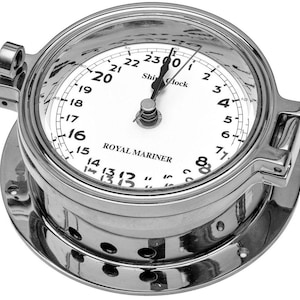 May include: A circular silver-toned metal ship clock with a white face, black numerals from 1 to 23, and black hands. The dial features the text "Ship Clock" and "ROYAL MARINER". The clock has a hinged frame with a latch and a mounting flange.