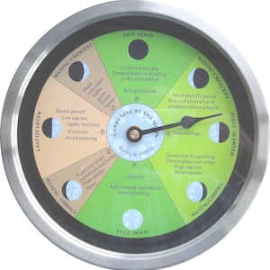 May include: A round, silver-framed clock with a green and tan face, featuring phases of the moon and gardening tips. The clock face includes text such as "Gardening by the Moon" and "Take cuttings."