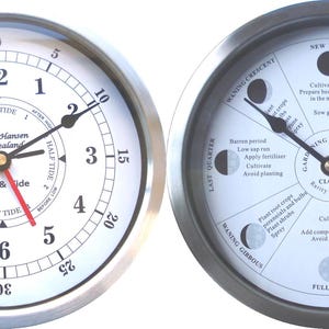 May include: Two silver-framed clocks with white faces. The clock on the left shows the time and tide, with a red hand indicating the tide level. The clock on the right is a gardening by the moon clock, with a black hand pointing to the waxing crescent moon phase. The clock face shows the different moon phases and gardening tasks for each phase.