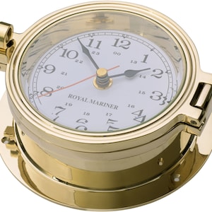 May include: A circular brass clock with a white face and black numerals, resembling a ship's porthole. The clock face features the words "ROYAL MARINER". It has a glass cover and a red second hand. The clock is designed to be mounted on a surface.