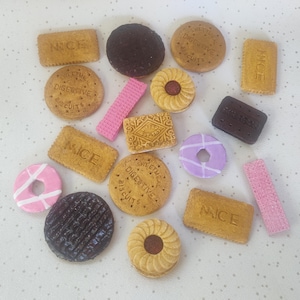 Puede incluir: Una colección de réplicas de galletas en miniatura que incluye galletas rectangulares Nice, galletas redondas Digestive, círculos y rectángulos de color chocolate oscuro, tiras de barquillo rosa, cremas de vainilla y galletas en forma de anillo.