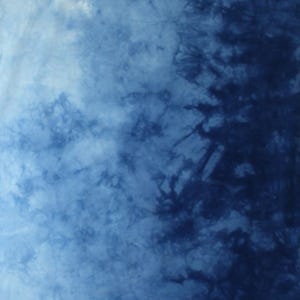 May include: A fabric featuring a tie-dye pattern with a gradient transition from light blue to deep navy blue. The design displays organic, branching, and cloud-like shapes created by the dye process. The letter C is visible in the bottom right corner.