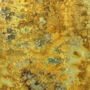May include: A fabric with a tie-dye pattern featuring shades of golden yellow, mustard, and deep brown, with scattered light blue and white accents throughout the design. The letter K is printed in white in the bottom right corner of the fabric.