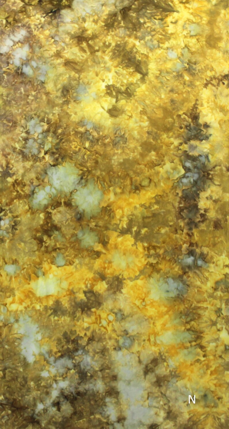 May include: A fabric featuring a tie-dye pattern in shades of golden yellow, mustard, brown, and off-white. The design displays organic, cloud-like clusters and mottled textures throughout the surface. The letter N is visible in the bottom right corner.