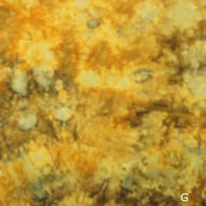 May include: A fabric surface featuring a mottled, tie-dye pattern in shades of golden yellow, ochre, and dark brown. The texture appears soft and uneven, with blended color transitions throughout the material. The letter G is visible in the corner.