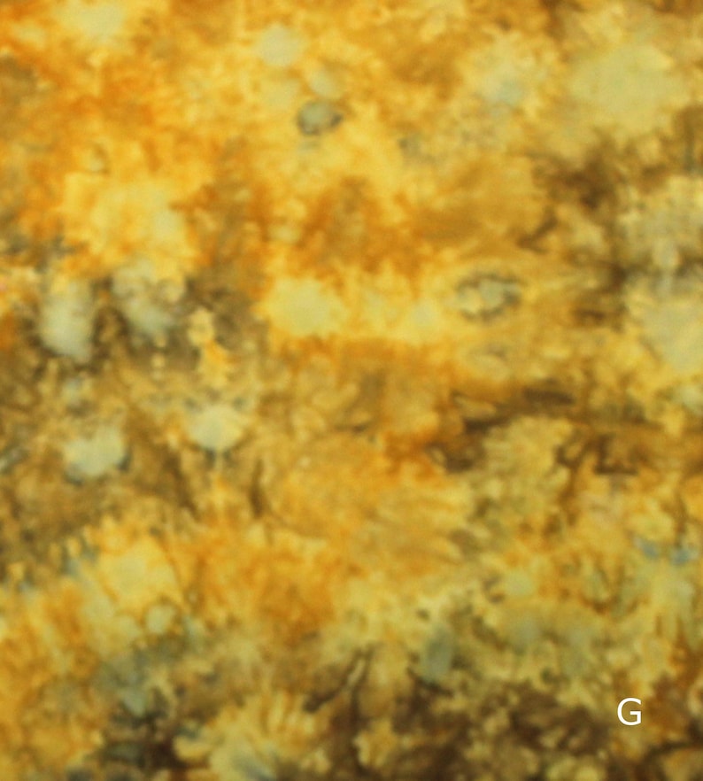 May include: A fabric surface featuring a mottled, tie-dye pattern in shades of golden yellow, ochre, and dark brown. The texture appears soft and uneven, with blended color transitions throughout the material. The letter G is visible in the corner.