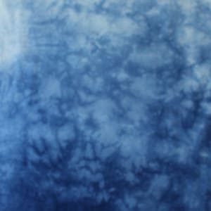 May include: A fabric featuring a tie-dye pattern with a gradient effect that transitions from a light, pale blue at the top to a deep, saturated navy blue at the bottom. The surface displays organic, cloud-like textures and the letters CC in white.