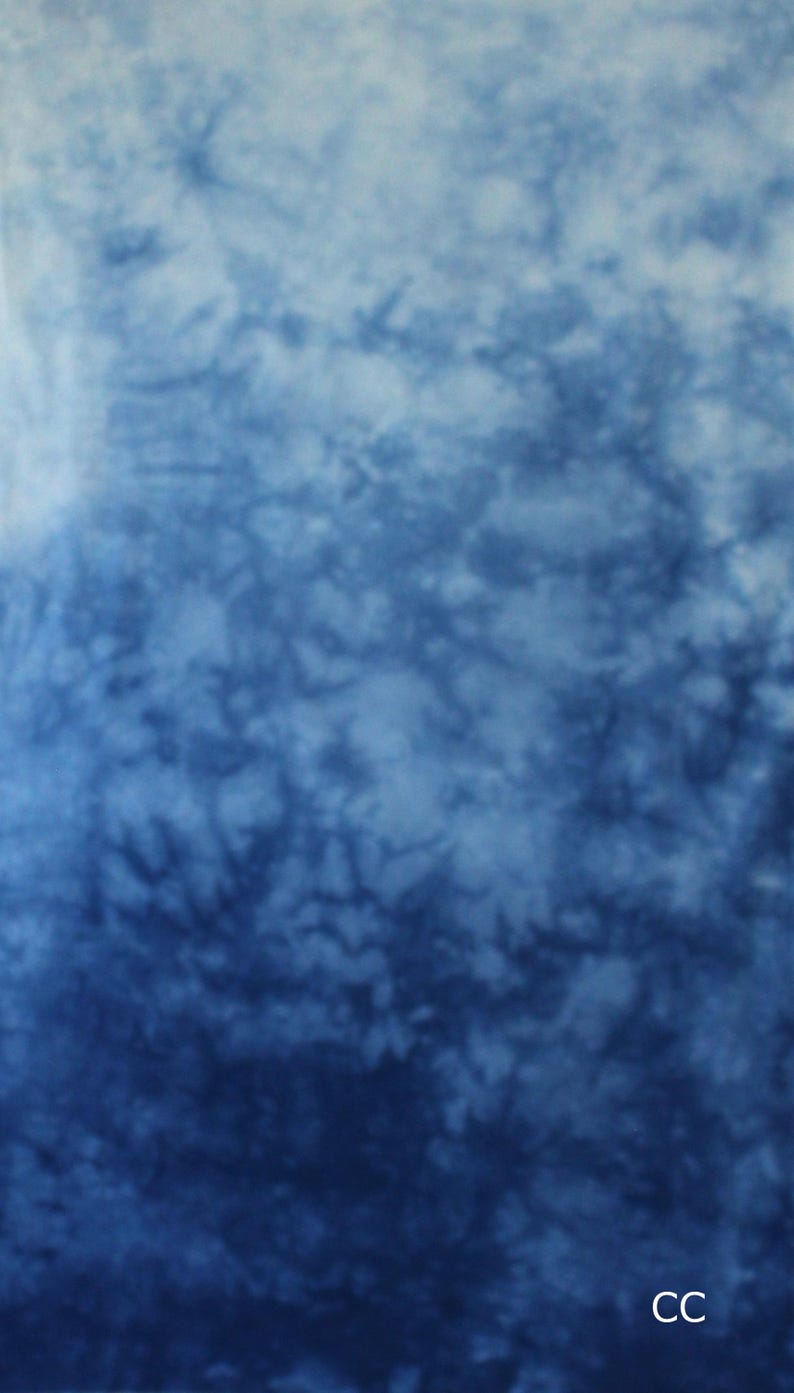 May include: A fabric featuring a tie-dye pattern with a gradient effect that transitions from a light, pale blue at the top to a deep, saturated navy blue at the bottom. The surface displays organic, cloud-like textures and the letters CC in white.