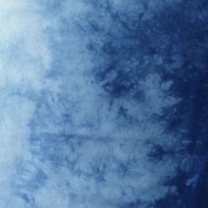 May include: A fabric featuring a tie-dye pattern with a gradient of deep indigo blue to light sky blue. The surface displays organic, cloud-like mottled textures and intricate branching shapes. The letter C is printed in white in the bottom corner.