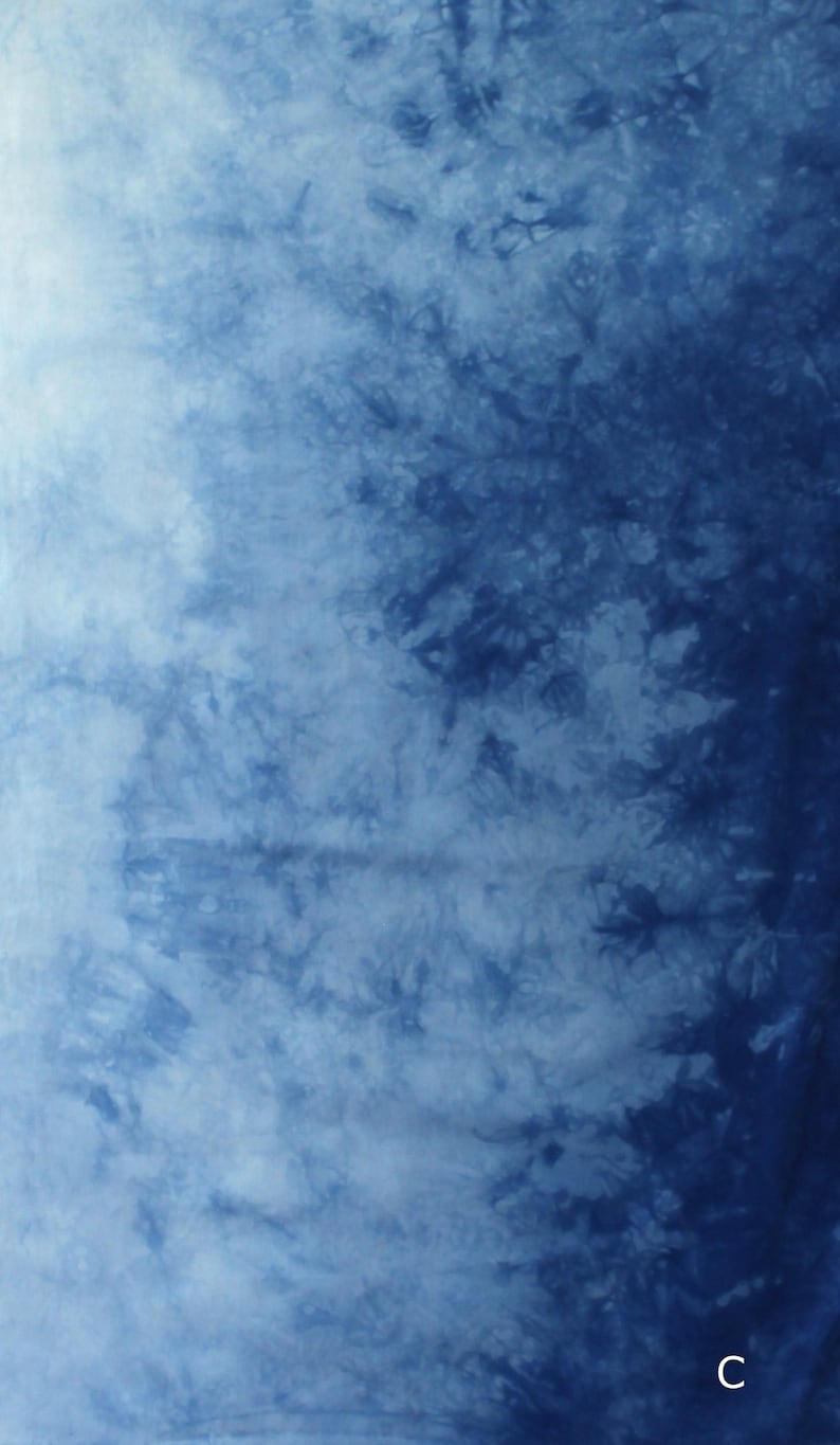 May include: A fabric featuring a tie-dye pattern with a gradient of deep indigo blue to light sky blue. The surface displays organic, cloud-like mottled textures and intricate branching shapes. The letter C is printed in white in the bottom corner.