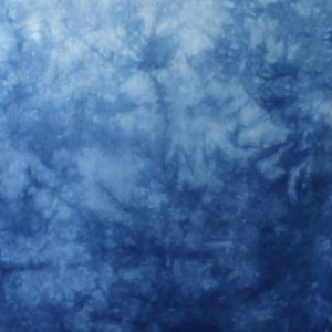 May include: A fabric featuring a tie-dye pattern in shades of blue and white, transitioning from a lighter blue at the top to a deeper, saturated indigo at the bottom. The letters AA are printed in white in the bottom right corner of the textile.
