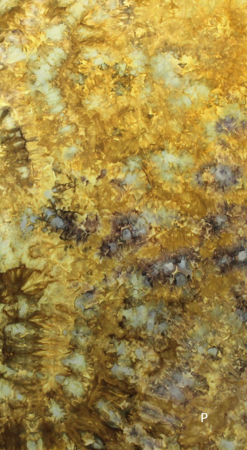 May include: A fabric surface featuring a tie-dye pattern with a blend of golden yellow, mustard, and deep brown hues, interspersed with patches of pale cream and white. The letter P is visible in the bottom right corner of the textile.