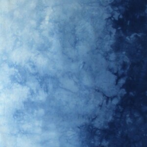 May include: A textile fabric featuring a tie-dye pattern with a gradient transition from light sky blue on the left to deep navy blue on the right. The surface displays organic, cloud-like mottled textures throughout. The letter D is visible.
