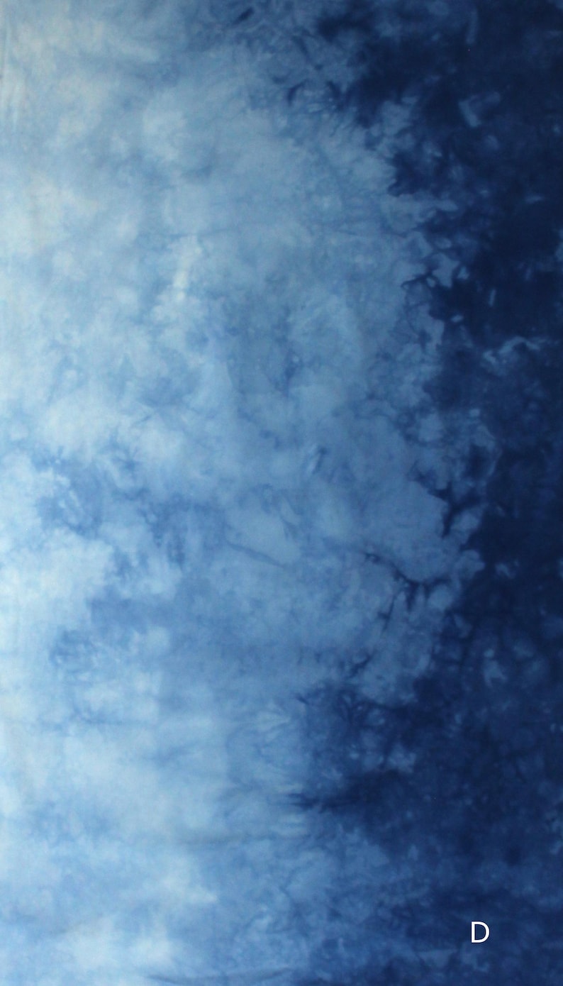 May include: A textile fabric featuring a tie-dye pattern with a gradient transition from light sky blue on the left to deep navy blue on the right. The surface displays organic, cloud-like mottled textures throughout. The letter D is visible.