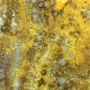 May include: A fabric textile featuring a tie-dye pattern in shades of mustard yellow, golden yellow, olive green, and muted gray. The design displays organic, mottled color transitions with concentrated areas of deep pigment and lighter patches.