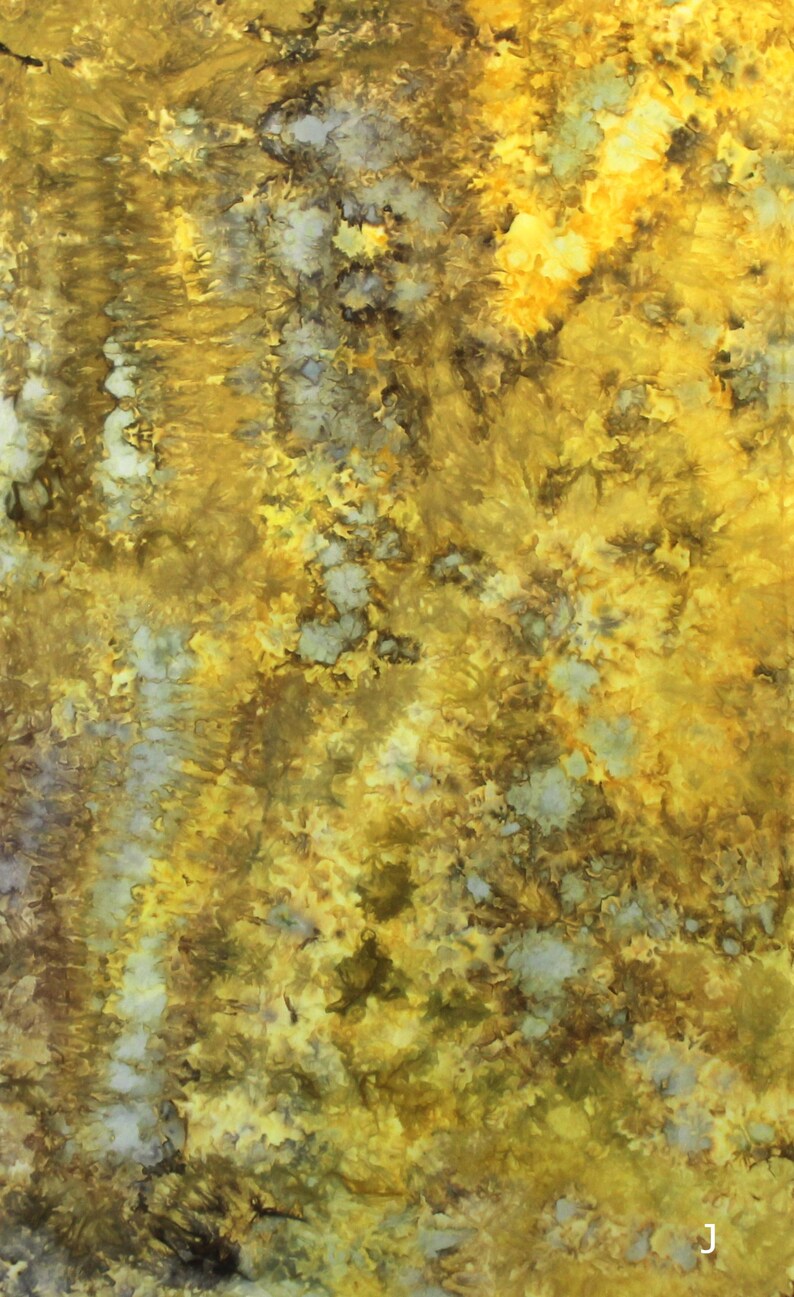 May include: A fabric textile featuring a tie-dye pattern in shades of mustard yellow, golden yellow, olive green, and muted gray. The design displays organic, mottled color transitions with concentrated areas of deep pigment and lighter patches.