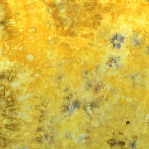 May include: A fabric surface featuring a tie-dye pattern with vibrant shades of yellow, gold, and mustard, accented by dark brown and charcoal gray mottled spots. The letter H is printed in white in the bottom right corner of the textile.