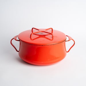 Könnte beinhalten: Ein leuchtend roter, emaillierter gusseiserner Dutch Oven mit passendem Deckel. Der Topf hat zwei Schlaufengriffe und einen Deckelgriff. Das Kochgeschirr ist für den Herd oder Backofen geeignet. Der Topf ist in einem leuchtenden Rot gehalten.