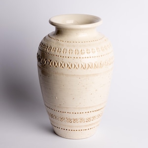 May include: A white ceramic mug with a black handle and the text "But First, Coffee" in a bold, black font. The mug is set against a blurred background, suggesting a cozy setting.