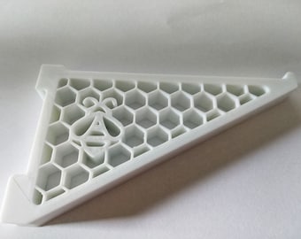 May include: White plastic shelf bracket with a honeycomb design and a bee silhouette. The bracket is triangular in shape.