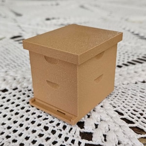 May include: A small, light brown wooden beehive with three sections. The beehive is made of wood and has a textured surface.