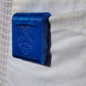 Puede incluir: Un objeto rectangular azul brillante con un dise&ntilde;o de abeja se coloca en un bolsillo blanco. El dise&ntilde;o de la abeja est&aacute; en relieve en la parte delantera. Probablemente sea un peque&ntilde;o contenedor o accesorio.