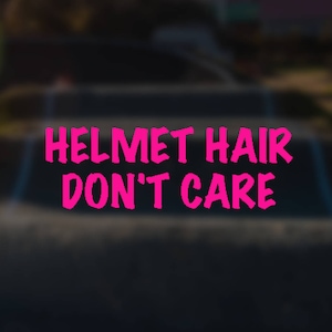 Pode incluir: Uma imagem desfocada de uma superfície preta com o texto "HELMET HAIR DON'T CARE" em letras cor-de-rosa.