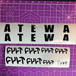 May include: Two white sheets of vinyl with black lettering. The top sheet has the word "GATEWAY" written twice in large, bold letters. The bottom sheet has the word "FULT" written eight times in a stylized font.